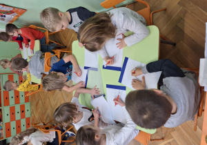 Na zdjęciu dzieci siedzą przy stolikach, projektują wnętrze swoich pokoi.