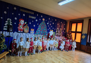 Na zdjęciu dzieci stoją z Mikołajem na tle dekoracji świątecznej.