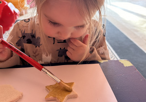Na zdjęciu dziewczynka maluje na złoto gwiazdkę z masy solnej.