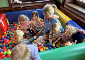 Na zdjęciu dzieci wraz z nauczycielką bawią się w basenie z kolorowymi kulkami.
