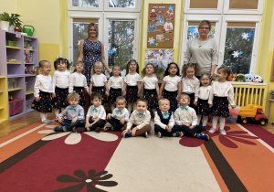 Na zdjęciu grupa dzieci wraz z nauczycielkami w odświętnych ubraniach przed występem z okazji Dnia Babci i Dziadka.