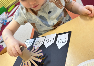 Na zdjęciu chłopiec wykonuje pracę plastyczną z użyciem farb i papierowej rolki.