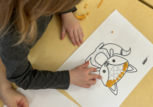 Na zdjęciu dziewczynka wykleja kontury liska pomarańczową plasteliną.