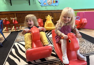 Na zdjęciu dwie dziewczynki podczas zabaw na bujanych konikach na przedszkolnej sali zabaw.