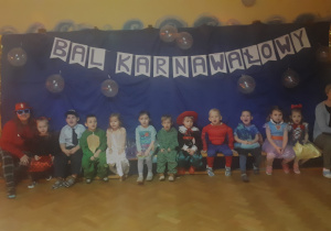 zdjęcie przedstawia dzieci z grupy ,,Misie” wraz z Paniami oczekujące na rozpoczęcie Balu Karnawałowego na sali gimnastycznej.
