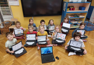 Dzieci pozujące do zdjęcia, w rękach trzymają laptopy wykonane z papieru.