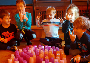 Dzieci siedzą na podłodze - przed nimi serce ułożone z różowych i pomarańczowych kubeczków