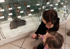 Na zdjęciu są dziewczynki oglądające z bliska skały znajdujące się w gablotach.