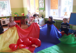 zdjęcie przedstawia dzieci z grupy ,,Misie” podczas zabawy w kole z wykorzystaniem chusty animacyjnej oraz balonów