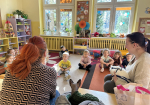 Na zdjęciu dzieci siedzą na dywanie i słuchają wolontariuszek z Fundacji Kocia Mama opowiadających o kotach.
