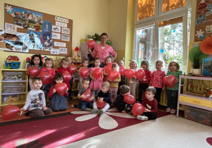 Na zdjęciu grupa wraz z nauczycielką pozują z czerwonymi balonami w kształcie serca.