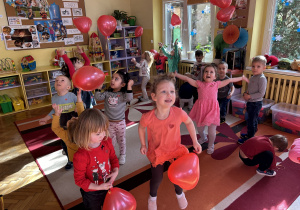 Na zdjęciu dzieci podrzucają czerwone balony w kształcie serca.
