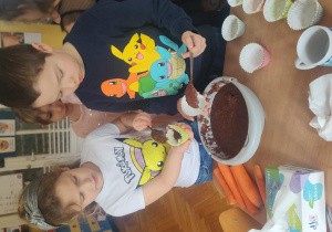Dziewczynka z chłopcem podczas nakładania surowego ciasta do foremki.