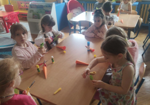 Dzieci siedzące przy stolikach podczas wykonywania pracy plastycznej - marchewka z papieru.
