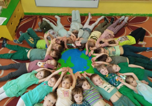 dzieci prezentują leżąc na podłodze wspólnie wykonaną pracę plastyczną