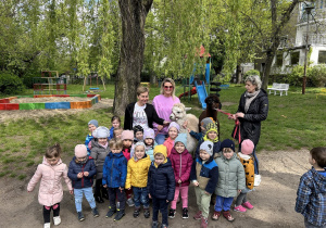 Na zdjęciu cała grupa Lisków pozuje w przedszkolnym ogrodzie w towarzystwie dwóch alpak.