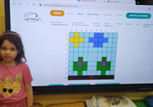 Dziewczynka prezentuje własny rysunek na tablicy multimedialnej.